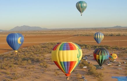 Hot air balloons of various colors and designs float over a desert landscape.