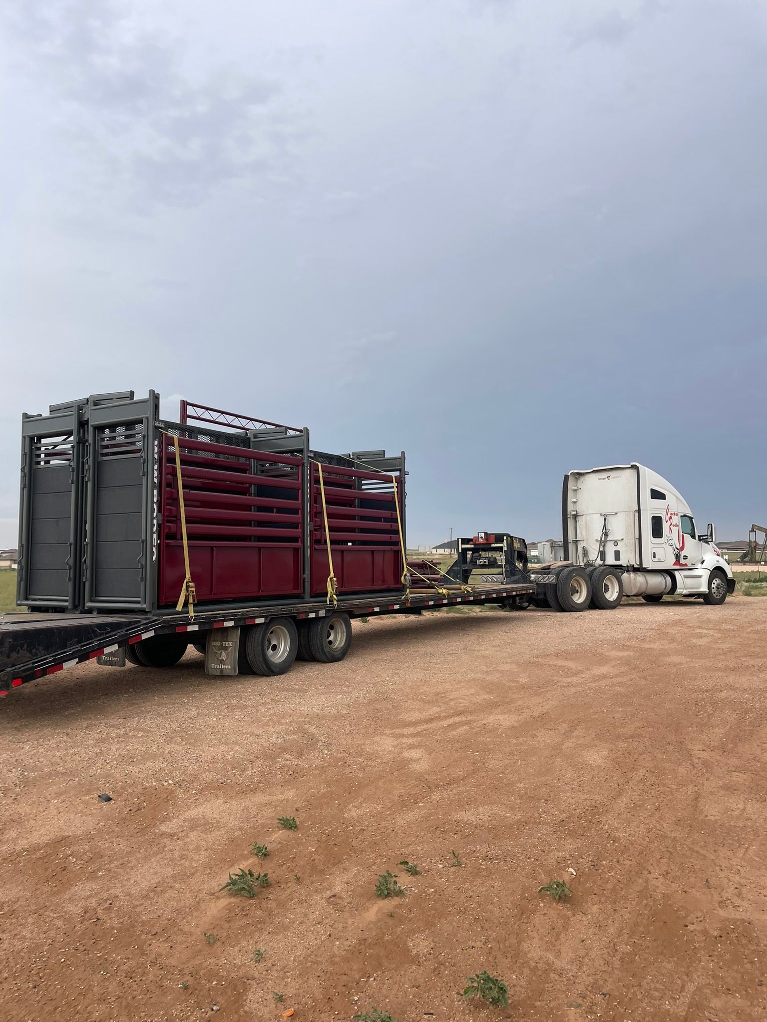Truck pulling a trailer with livestock handling equipment on a dirt road under a cloudy sky.