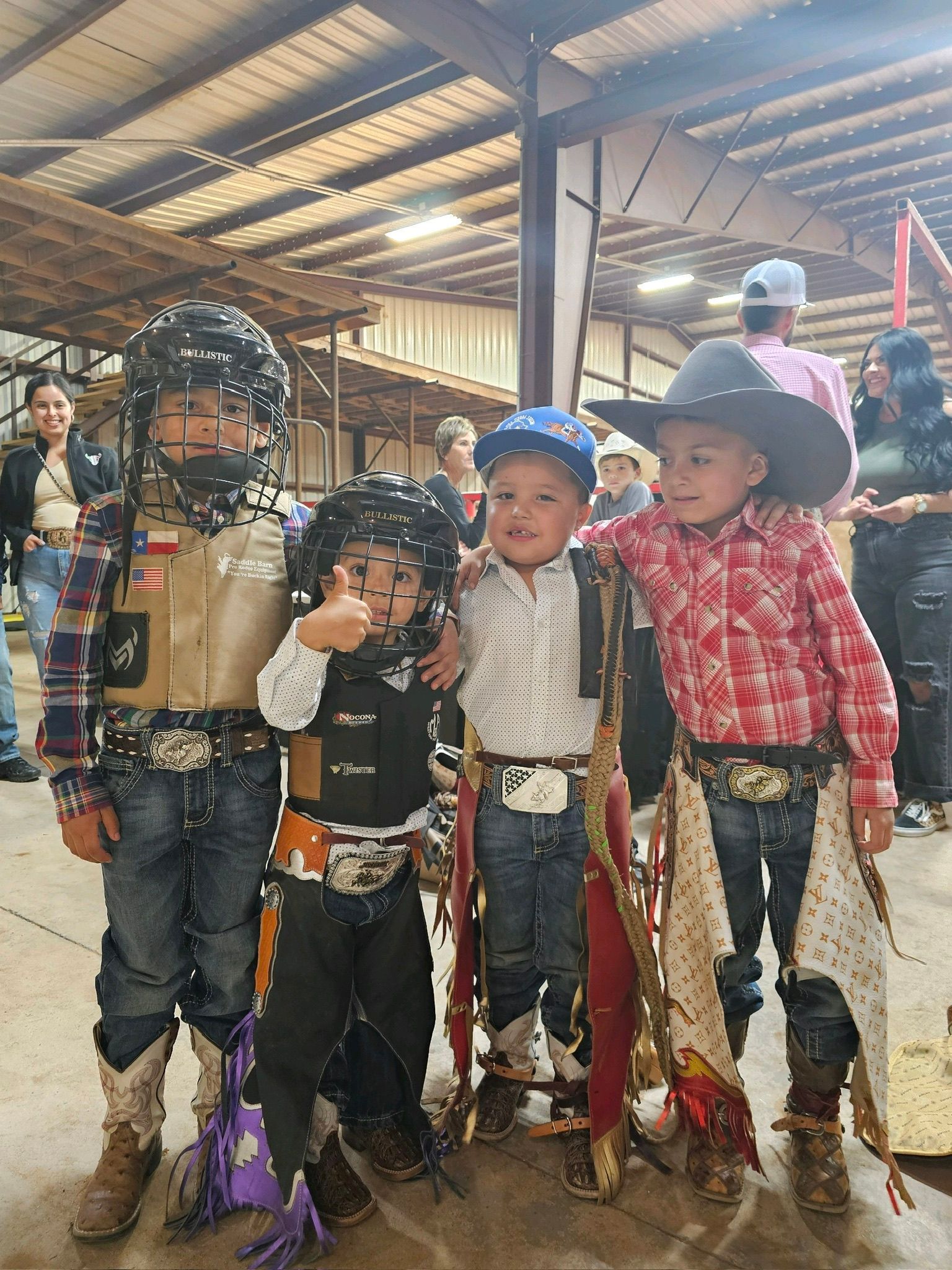Four children in cowboy attire pose for a photo inside a building; two wear protective gear.