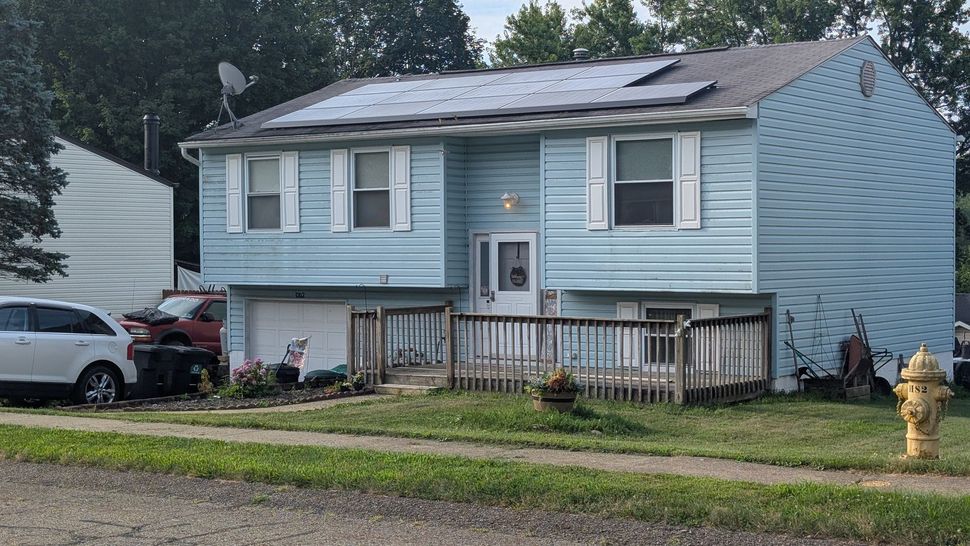 A blue house with solar panels on the roof and a fire hydrant in front of it.
