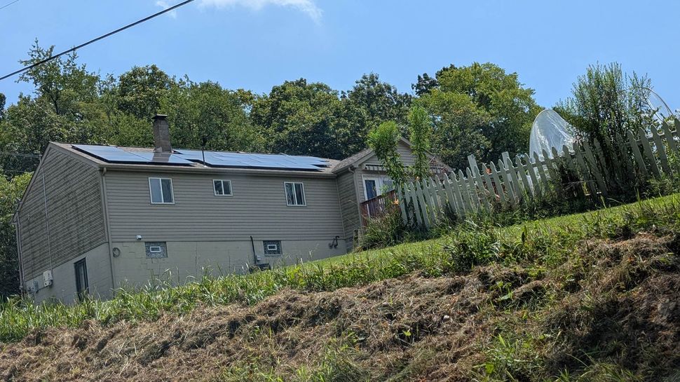 A house with solar panels on the roof is surrounded by trees and grass.