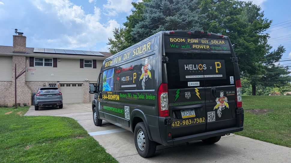 A black van with solar panel advertising parked in a driveway. The van's graphics include green and yellow lightning bolts and a superhero-like character.