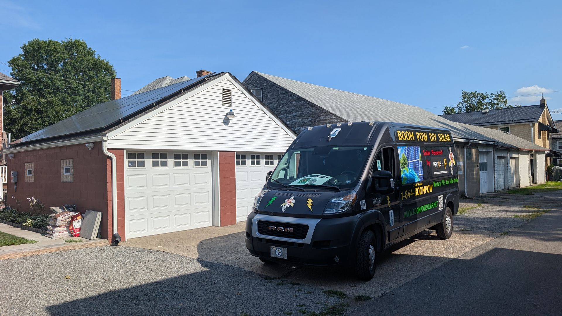 A black van parked in front of a garage with solar panels on the roof. The garage is red brick with a white garage door.