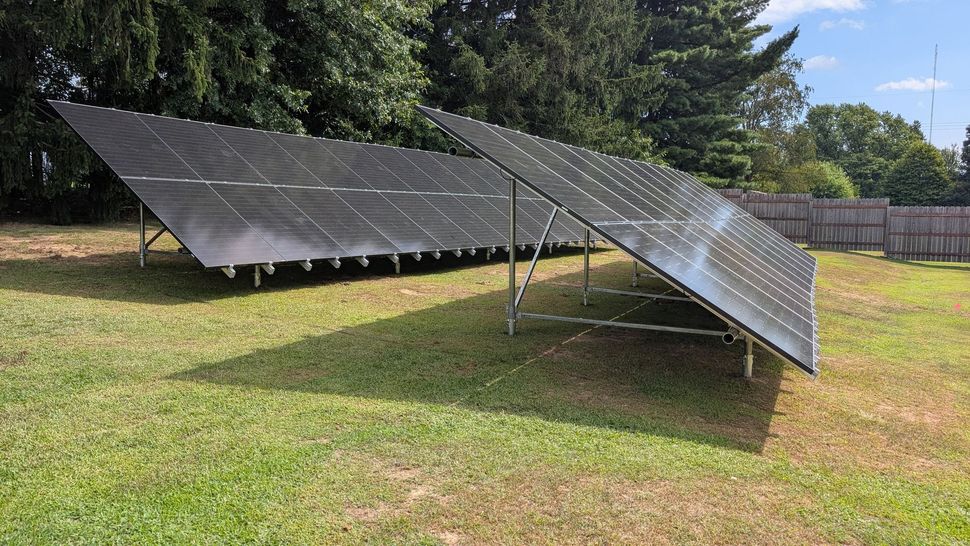 Ground-mounted solar panels in a grassy yard, angled towards the sun.