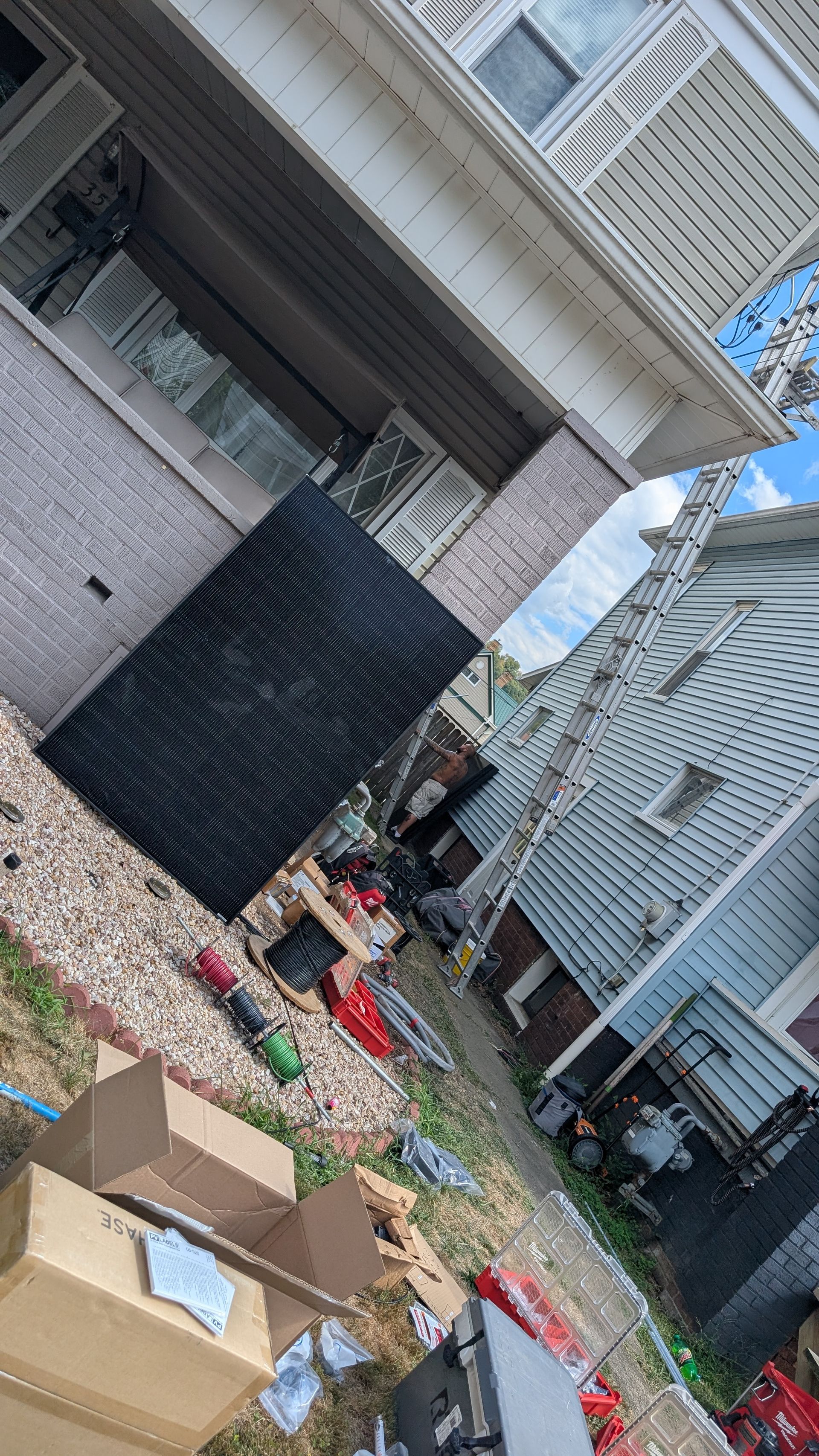 Exterior of a house with yard debris, including boxes and red items. Black screen. Blue sky.