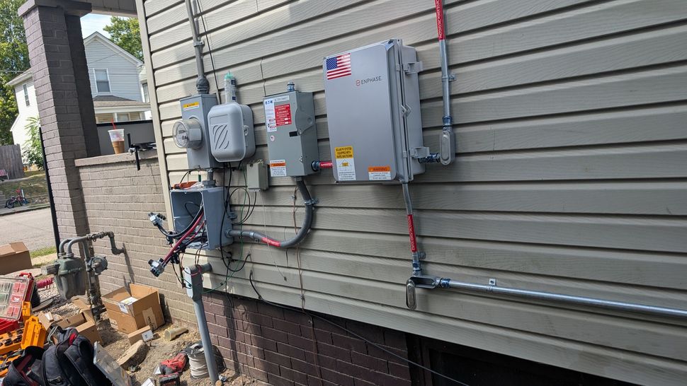 Electrical panel and conduits on a house's siding, with wires running between them.