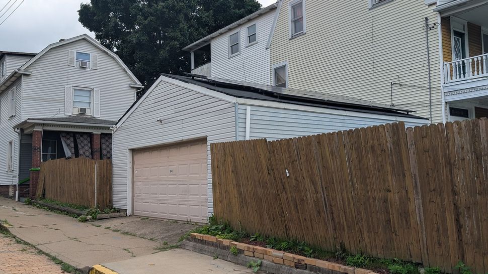 White garage with pink door beside wooden fence and houses on a cloudy day