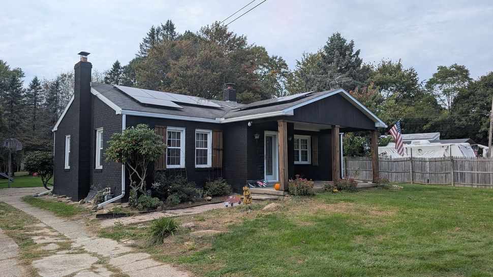 Black bungalow house with a covered porch and chimney beside a grassy yard and dirt driveway