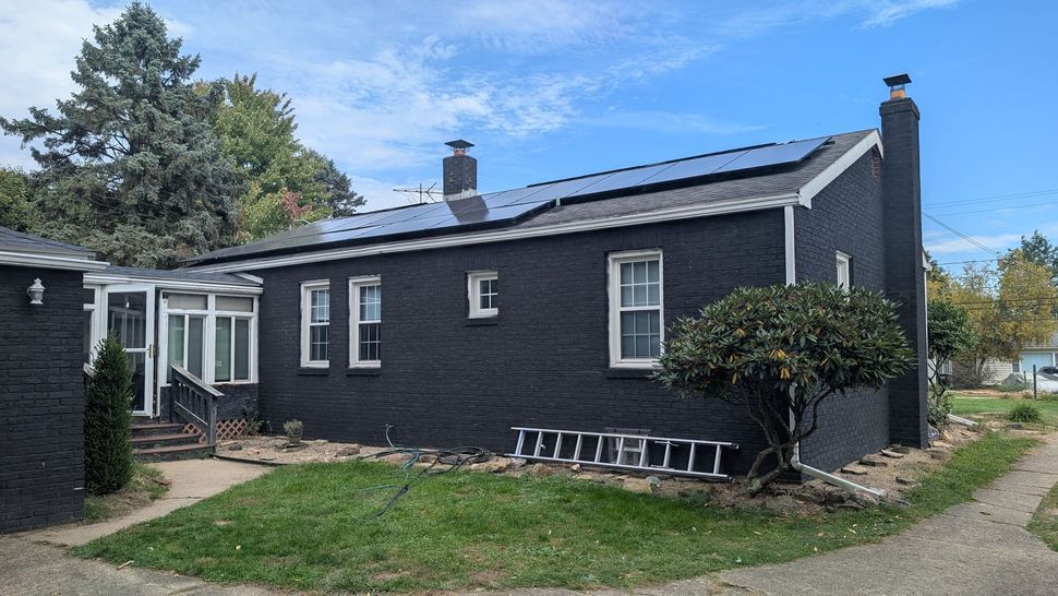 Black single-story house with white trim, front door steps, and a ladder leaning along the side.