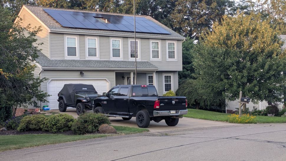 A black truck is parked in front of a house with solar panels on the roof.