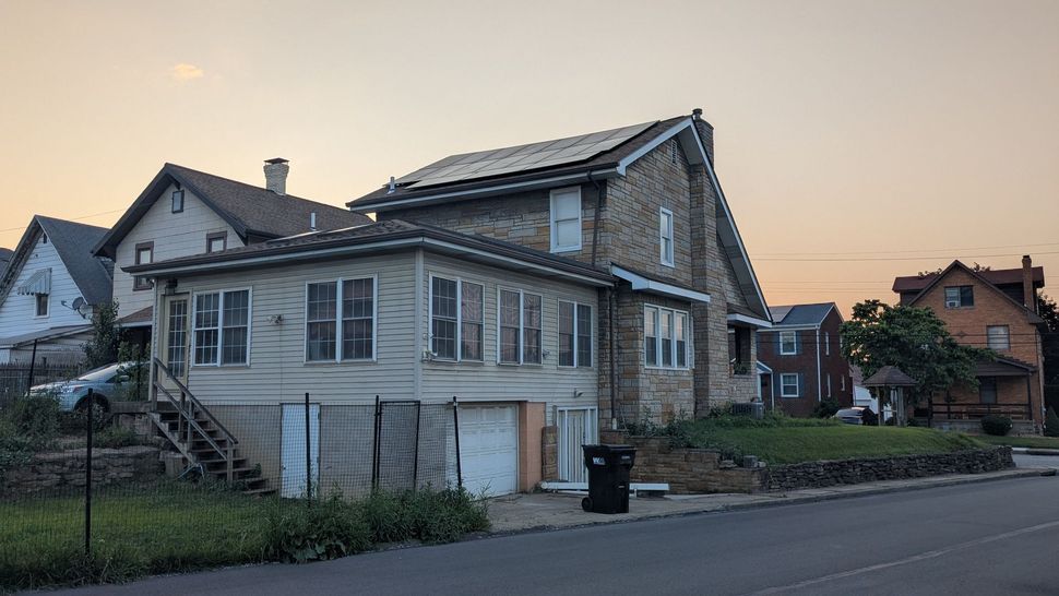 A house with solar panels on the roof is sitting on the side of the road.