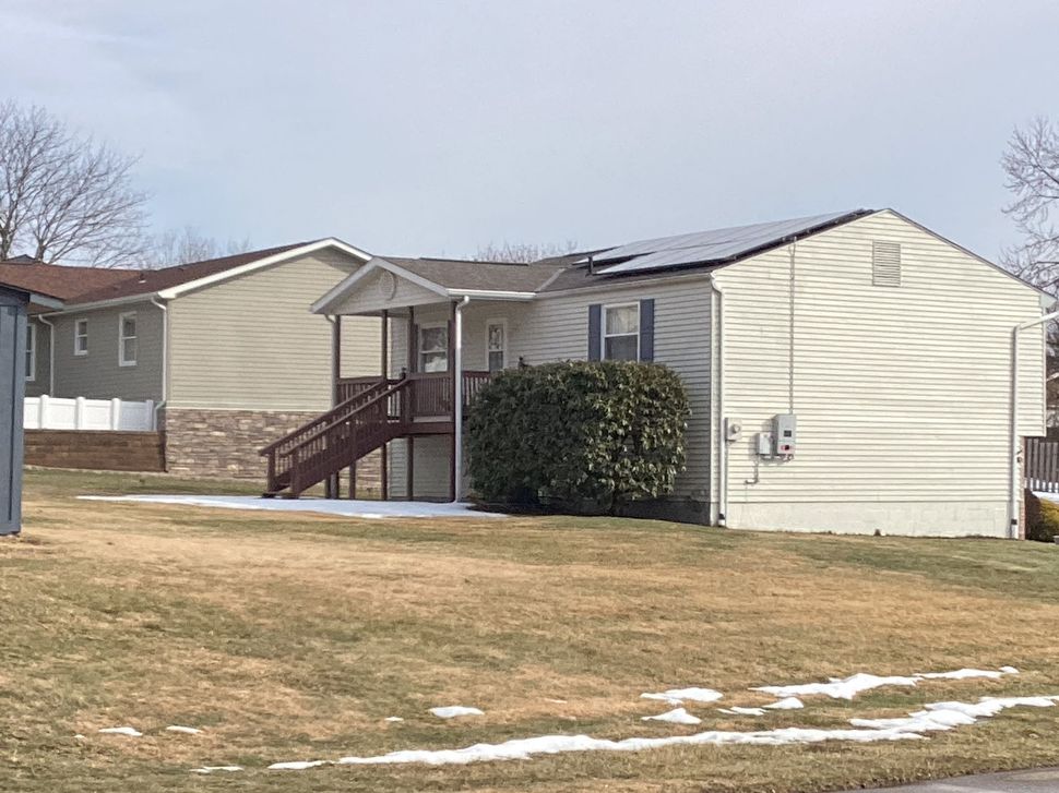 Single-story beige house with a small front porch and brown steps in a grassy yard with patches of snow