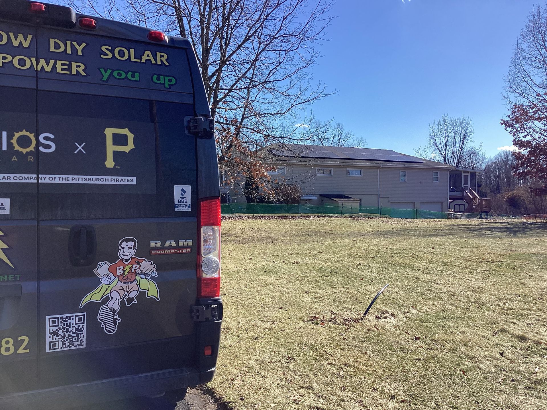 Black van with solar power advertisements parked on grass, house with solar panels in background.