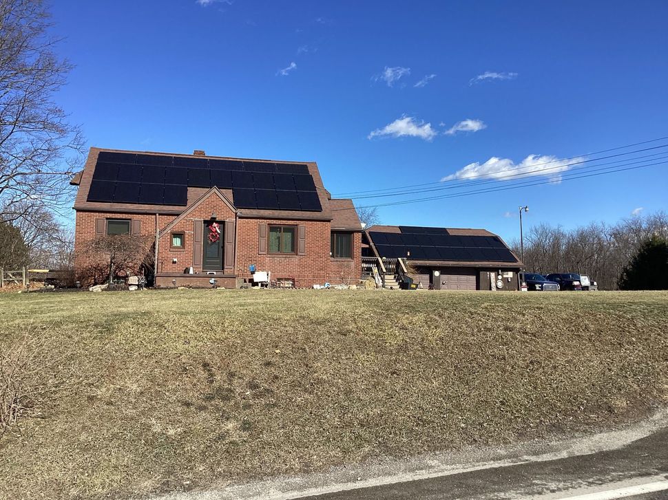 Brick house with dark roof on a grassy hill under a bright blue sky