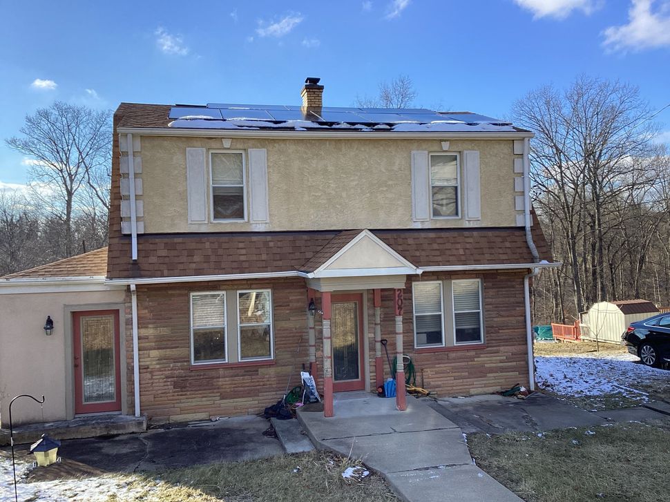Two-story house with brick and tan stucco exterior, porch, and a patch of snow on the roof.