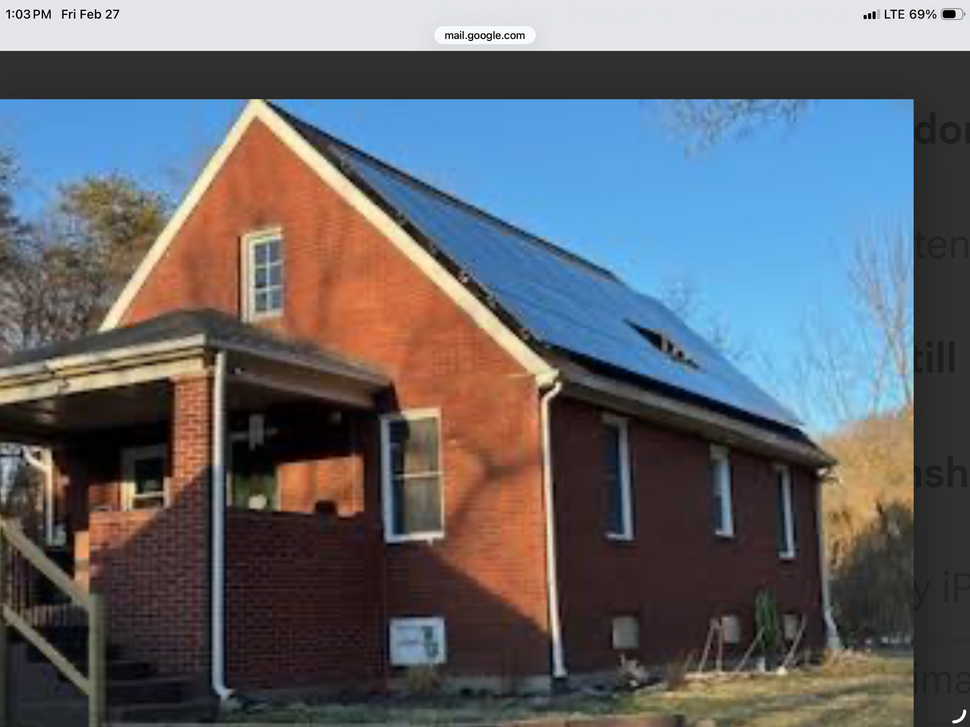 Red brick house with a steep roof and solar panels, viewed from the front under a clear blue sky