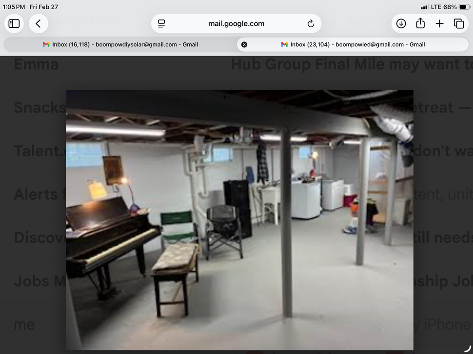 Basement room with a piano, chair, shelves, and water heater under exposed ceiling beams.