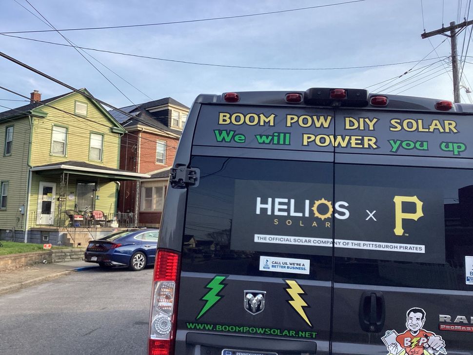 Black utility van with solar power ads parked on a street with houses in the background
