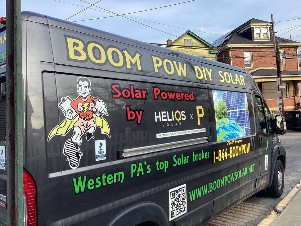 Black promotional van for Boom Pow Solar with bright graphics and text parked on a street