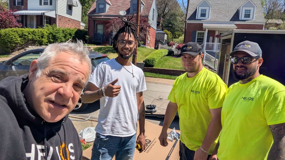 Four men posing together on a sunny suburban street, two wearing neon yellow shirts, with houses in the background