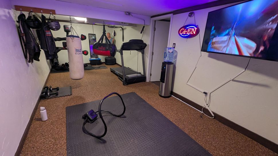 Home gym with a punching bag, treadmill, TV, and water cooler.