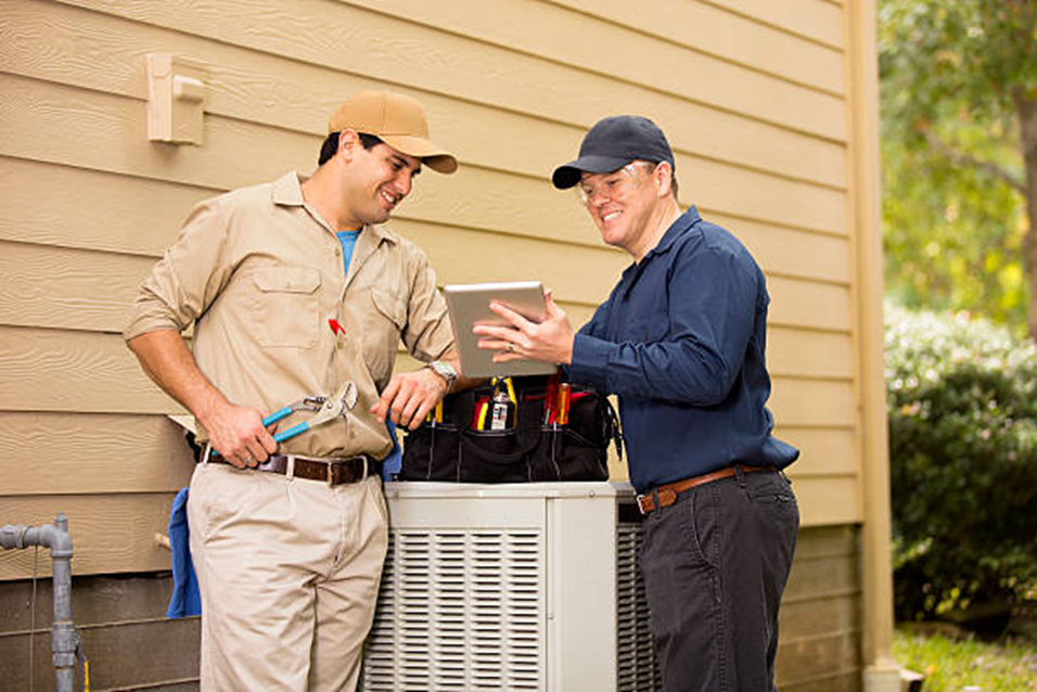 Two technicians examining a tablet, near an air conditioning unit outside a building on Long Island.