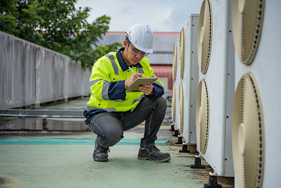 HVAC technician inspecting rooftop air conditioning units on Long Island, taking notes on a tablet.
