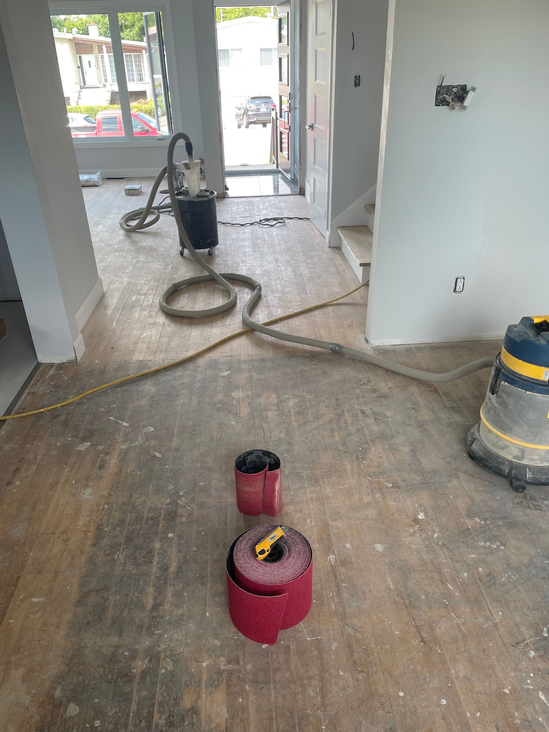 Ponçage de parquet en cours : une pièce avec du matériel de ponçage, du bois clair et des murs non finis.