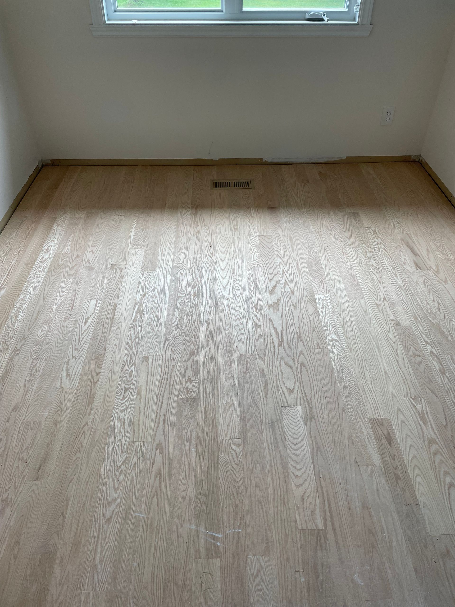 Parquet clair dans une pièce, sous un mur et une fenêtre blancs.