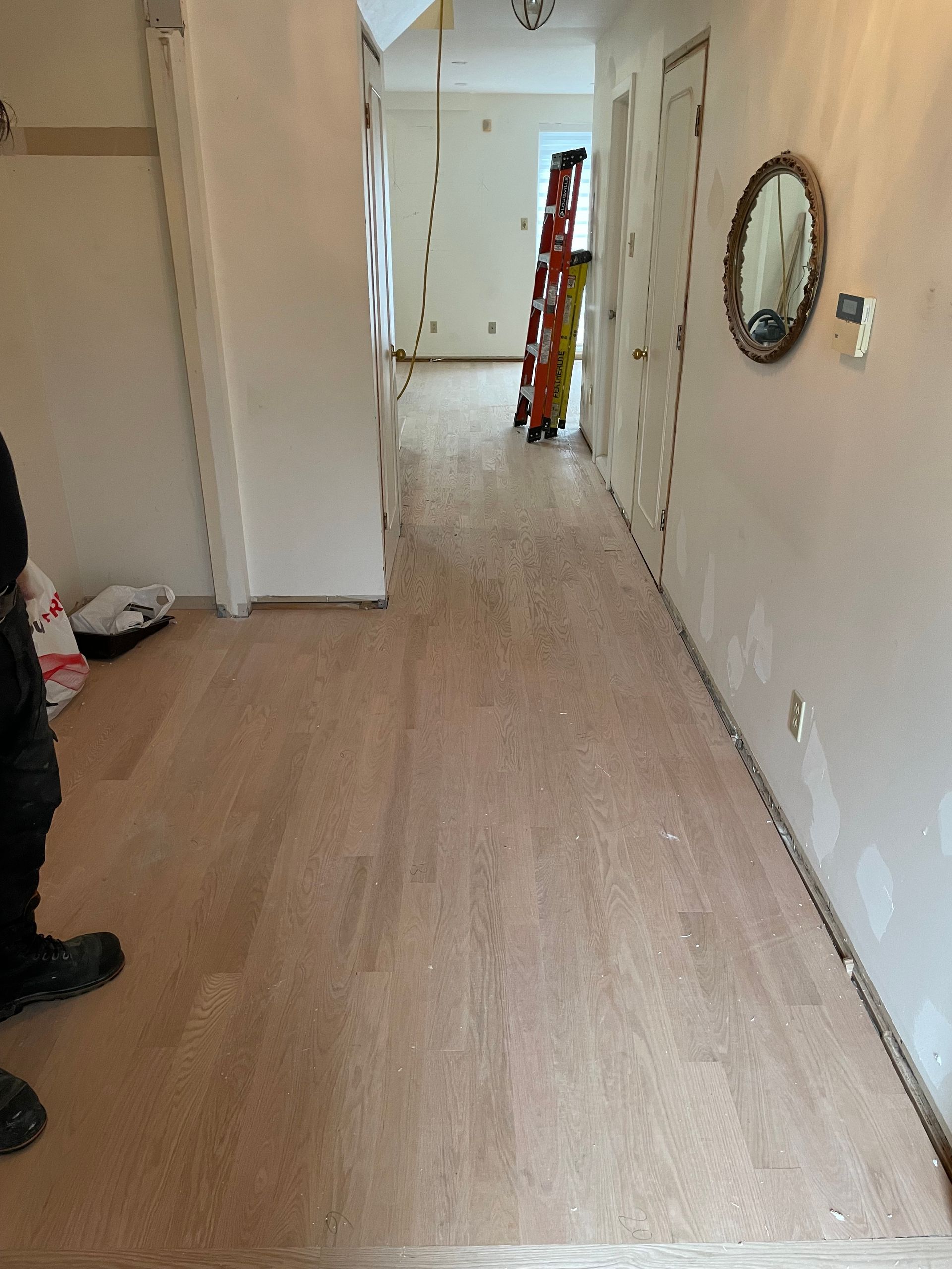 A person is standing in a hallway with a ladder and a mirror on the wall.
