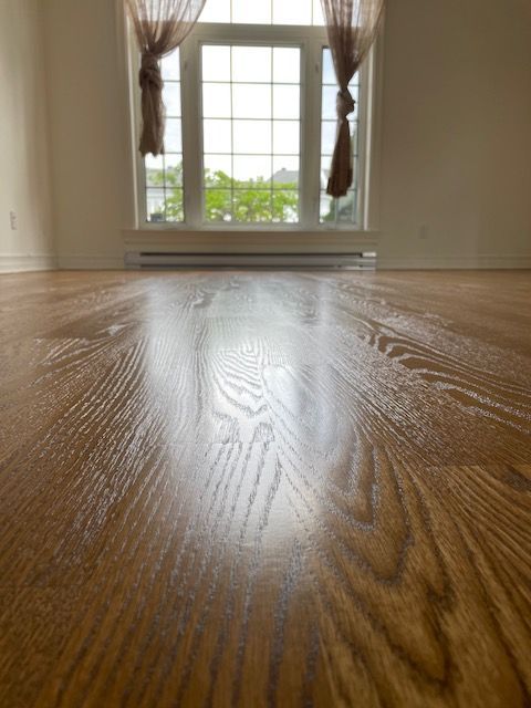 Gros plan sur un parquet brillant fraîchement rénové, avec une fenêtre lumineuse en arrière-plan.