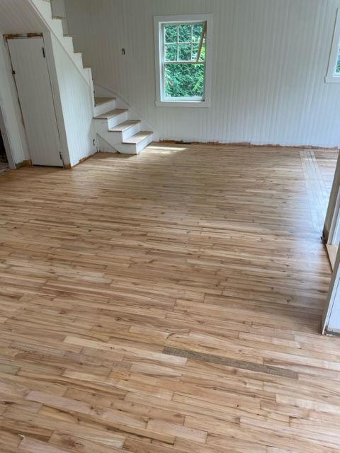 Parquet clair dans une pièce aux murs blancs, avec un escalier et une fenêtre.