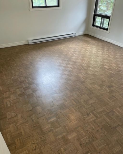 An empty room with a wooden floor and two windows.