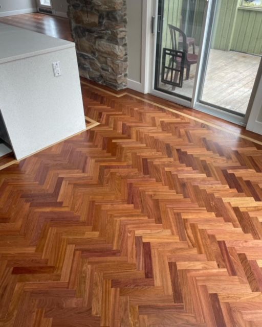 A wooden floor with a herringbone pattern in a room with a sliding glass door.