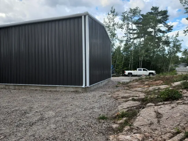A white truck is parked in front of a large metal building.