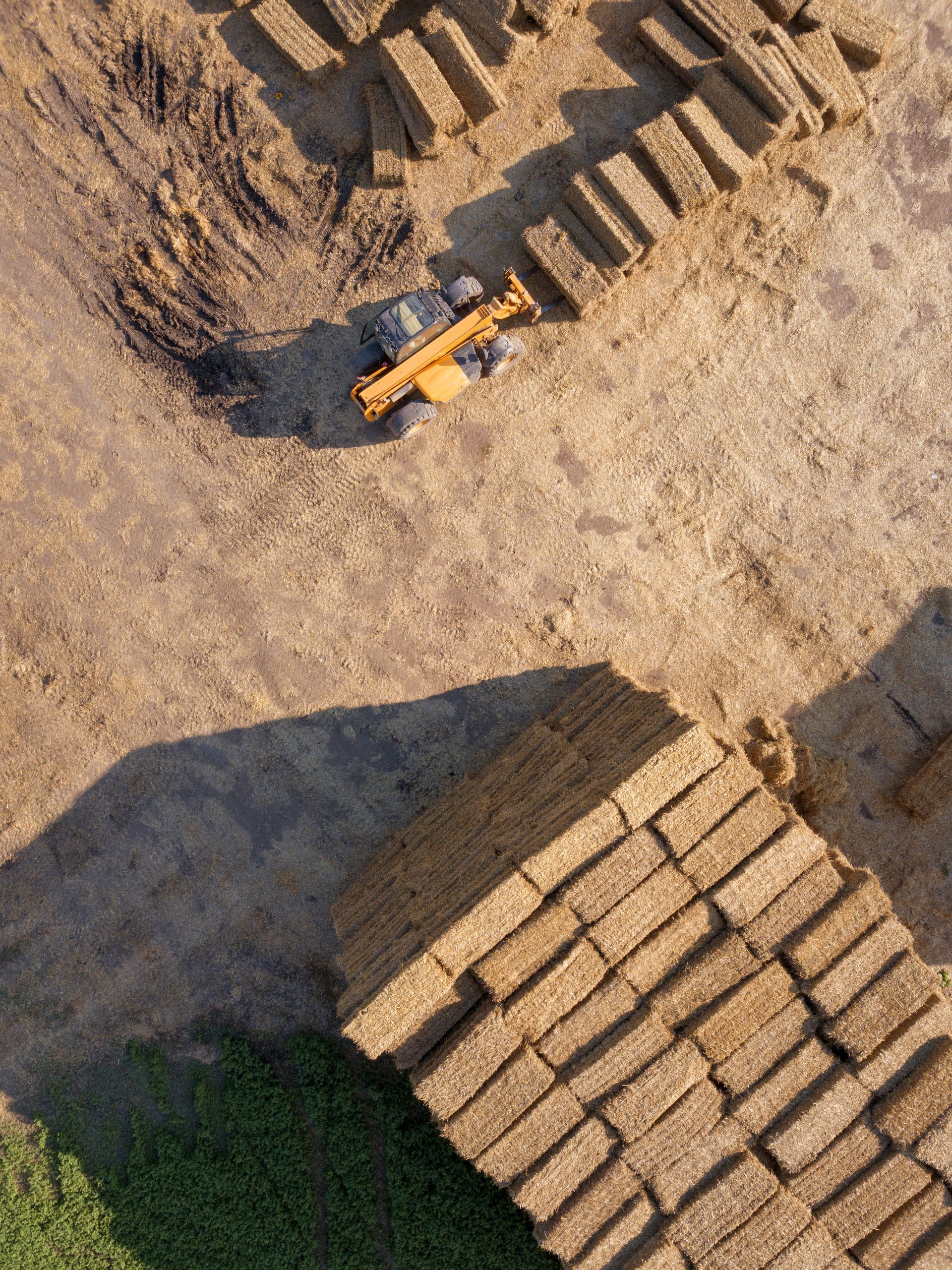 An aerial view of a bulldozer moving hay bales in a field.