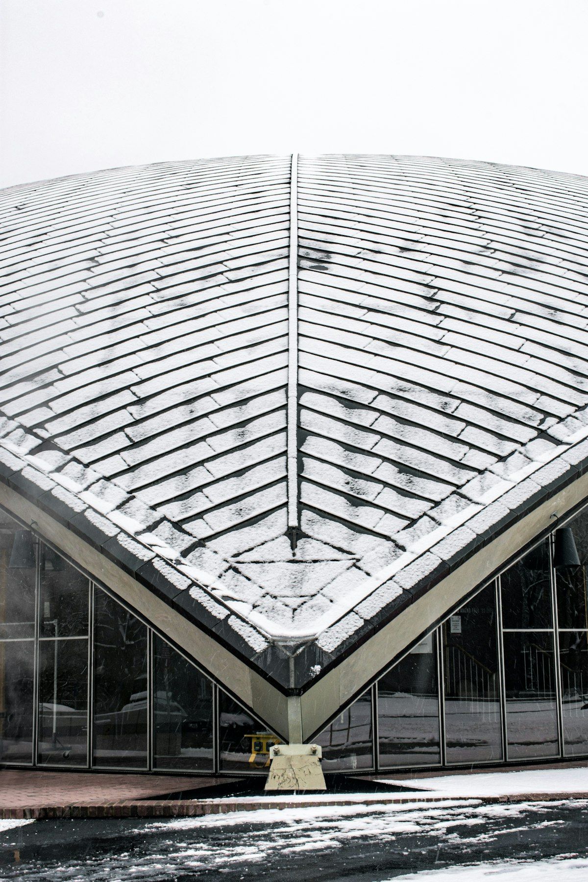 Snow-covered modern glass-roof building with a sharp triangular peak and symmetrical facade