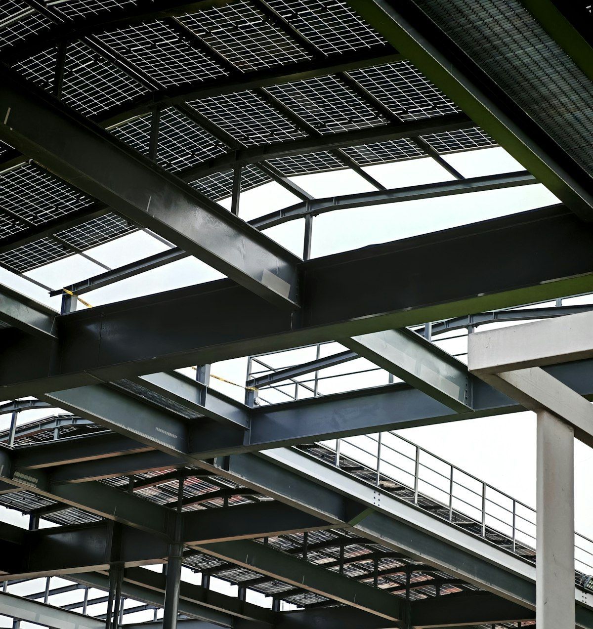 Steel bridge beams and grating viewed from below, with railings and bright sky above
