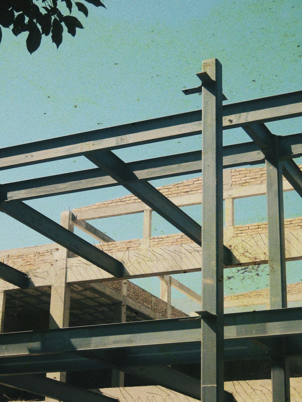 Partial view of a steel building frame under construction against a pale blue sky