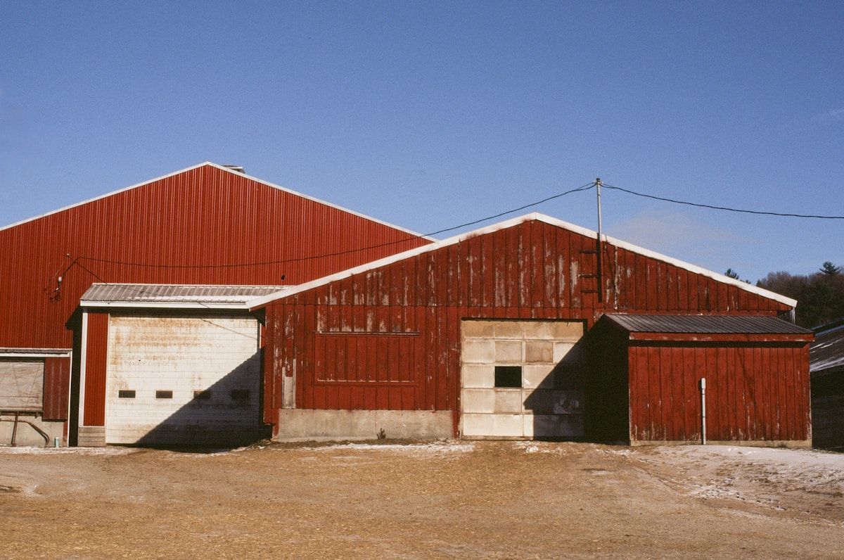 Red barn with white garage doors on a gravel lot under a clear blue sky