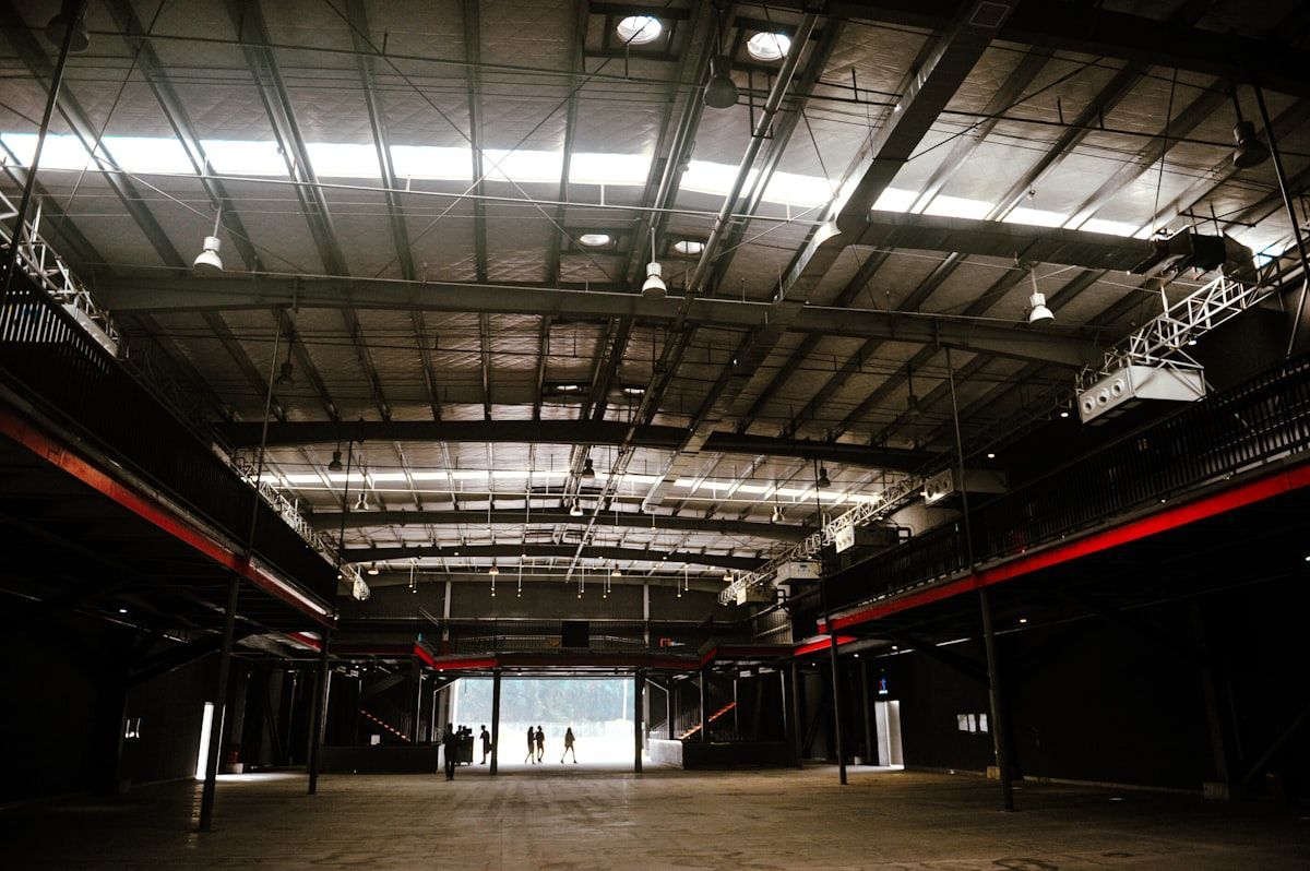 Empty industrial hall with a high metal ceiling and a bright doorway at the far end