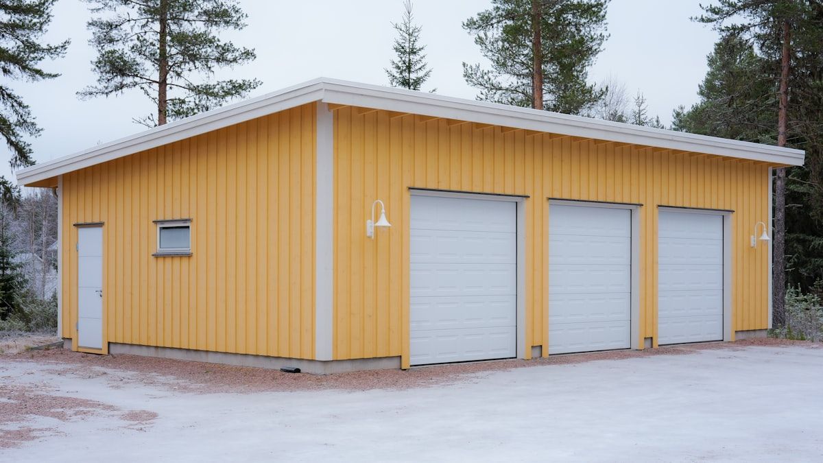 Yellow garage building with three white doors in a snowy outdoor setting