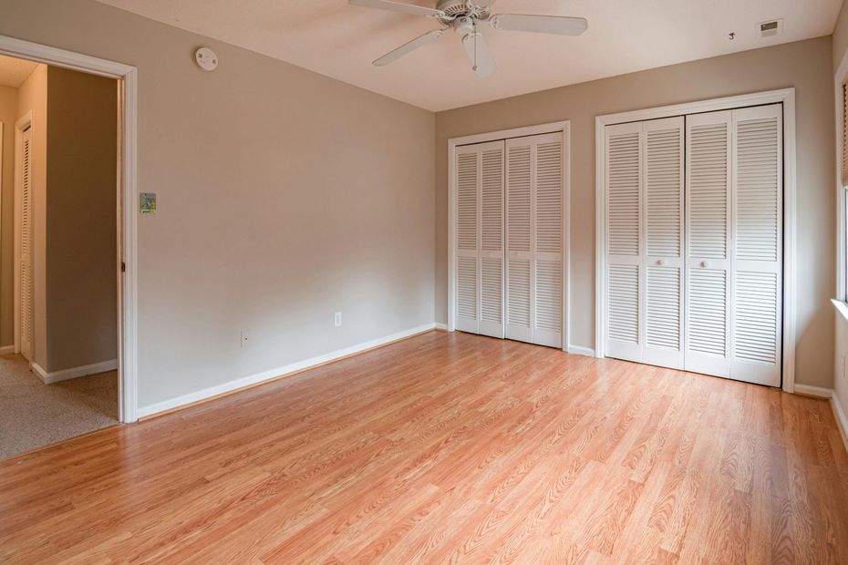 Empty room with hardwood floors, beige walls, two white closet doors, and an open doorway.
