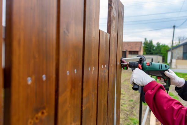 A man is installing a wood fence with a drill.