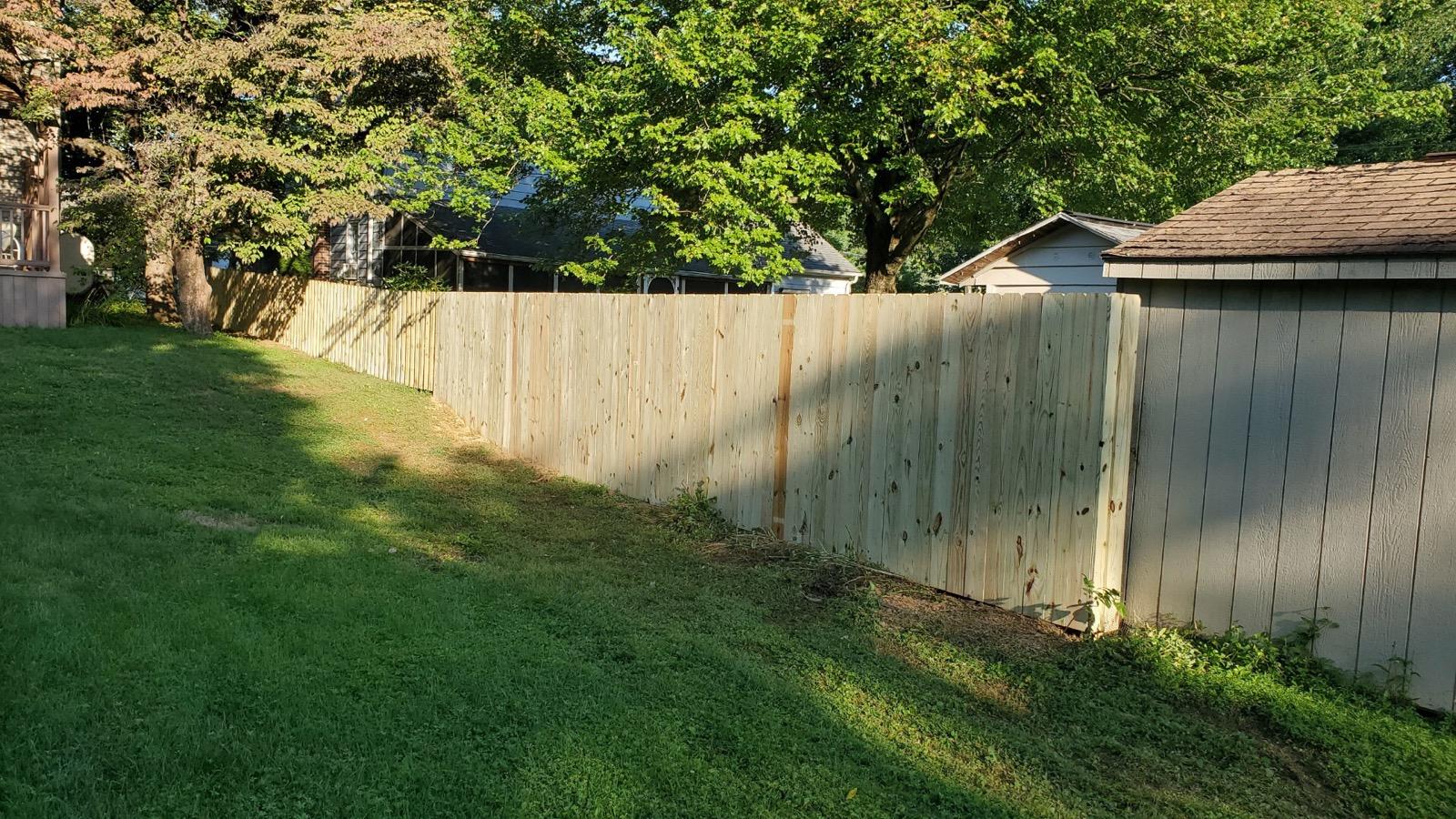 Wooden fence in a grassy yard, with trees in the background.