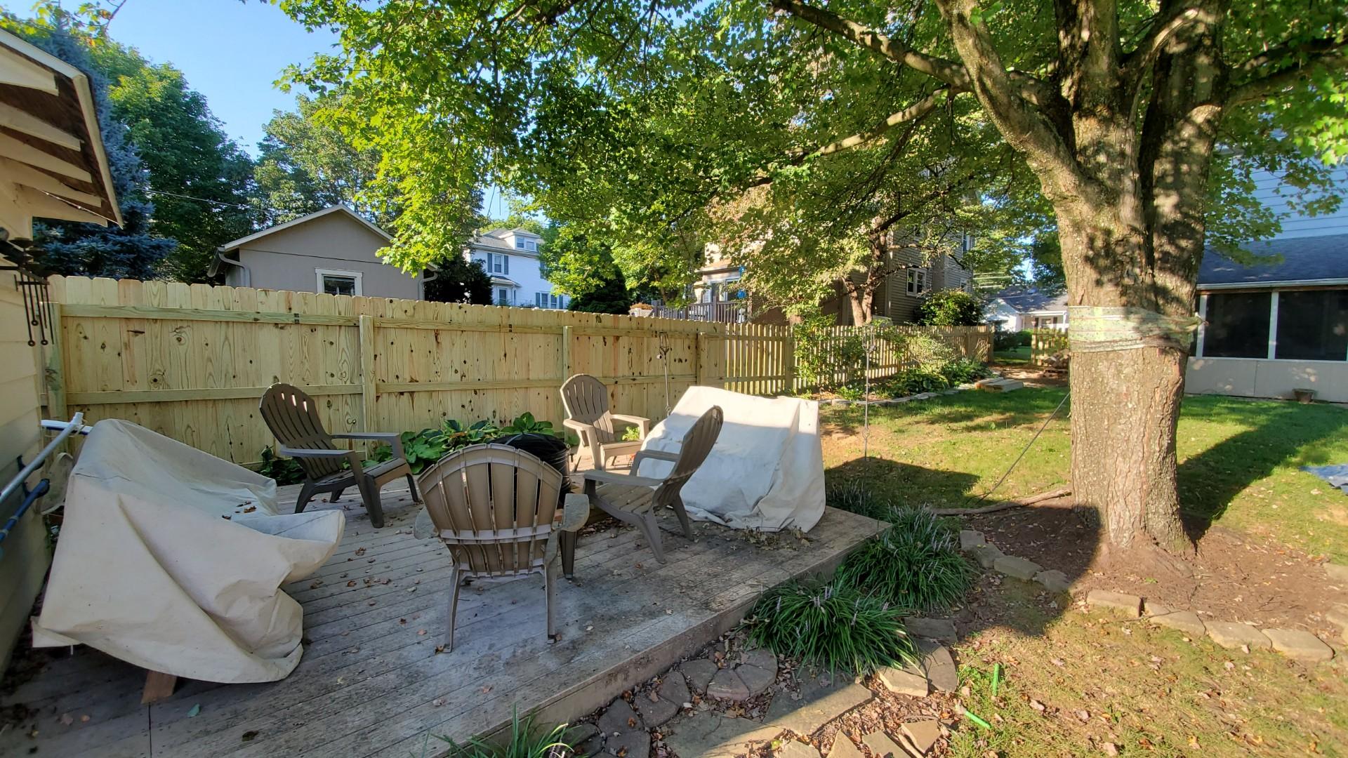 Backyard patio with chairs, a fence, and a large tree.