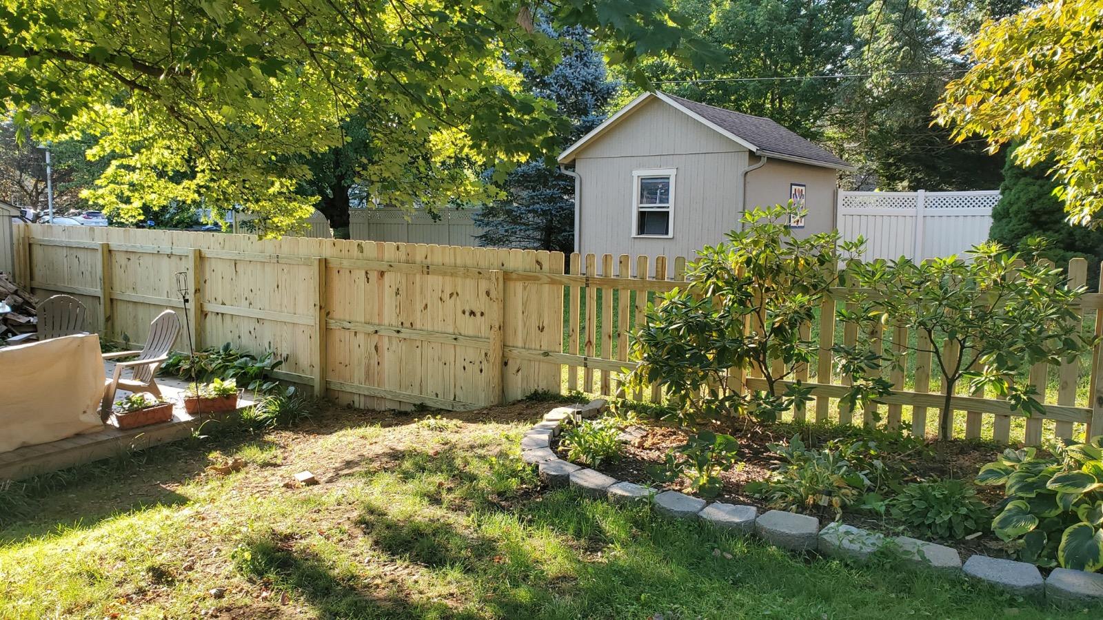 Backyard with a wooden fence, a shed, trees, and a garden.