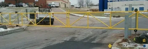 Yellow security gate blocking a driveway with a truck in the background.