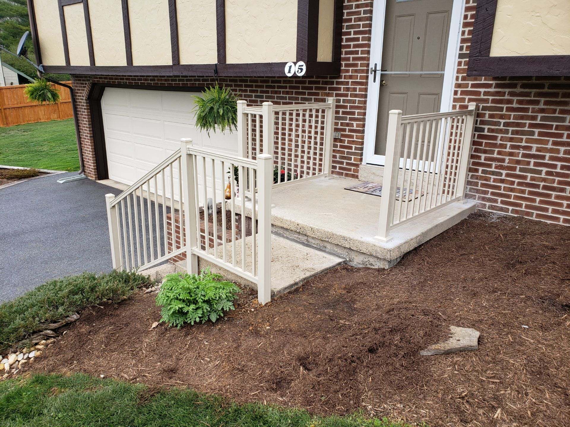Beige railing and steps leading to a home's front door; brown mulch and green lawn in the foreground.