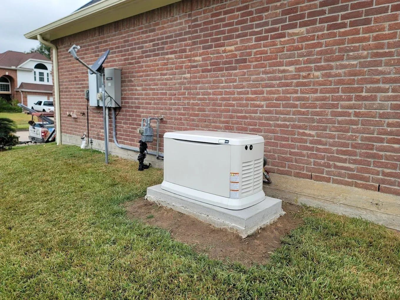 Outdoor standby generator beside a brick house on a concrete pad, near electrical meters and conduit